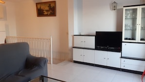 Ein Wohnzimmer mit einer Couch, einem Glastisch, einem Fernseher auf einem Schrank und einem Schrank mit Glastüren.