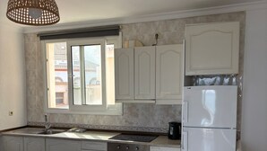 Eine Küche mit weißen Schränken, einem Edelstahlbackofen, einem weißen Kühlschrank und einem Esstisch mit Stühlen.