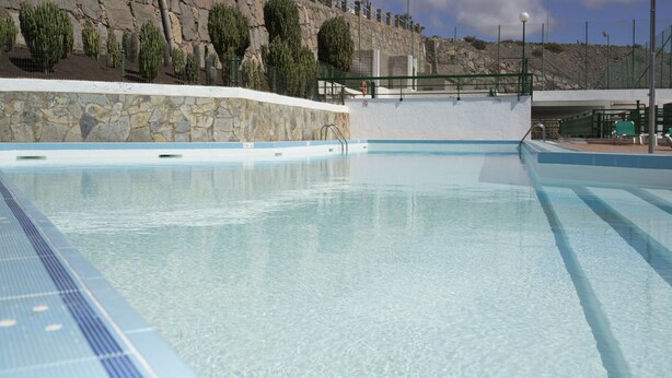 Ein klares Schwimmbecken mit einer Steinmauer und einer felsigen Hanglandschaft im Hintergrund.