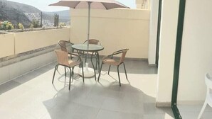 Ein Balkon mit rundem Tisch und Stühlen, einem großen Sonnenschirm und Blick auf einen Berg.