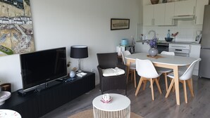 A modern living room with a flat-screen TV, a dining table with chairs, a kitchen area with cabinets and appliances, and a painting on the wall. - Les Plus Hautes Falaises d' Europe (Criel-sur-Mer)
