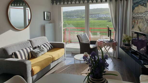 A living room with a sofa, a round mirror, a table with a computer, and a view of a green landscape through large windows. - Les Plus Hautes Falaises d' Europe (Criel-sur-Mer)
