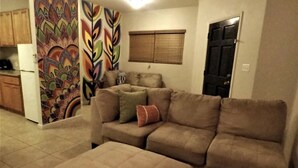 Una sala de estar con un sofá color beige, un reposapiés a juego y un llamativo cuadro abstracto en la pared.