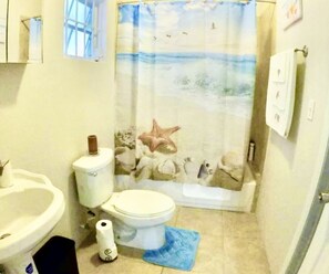 A bathroom with a toilet, sink, and shower curtain depicting a beach scene.