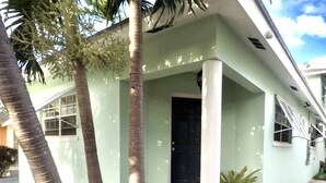 Un edificio de una sola planta con techo plano, puerta frontal negra y un pequeño porche con una maceta.