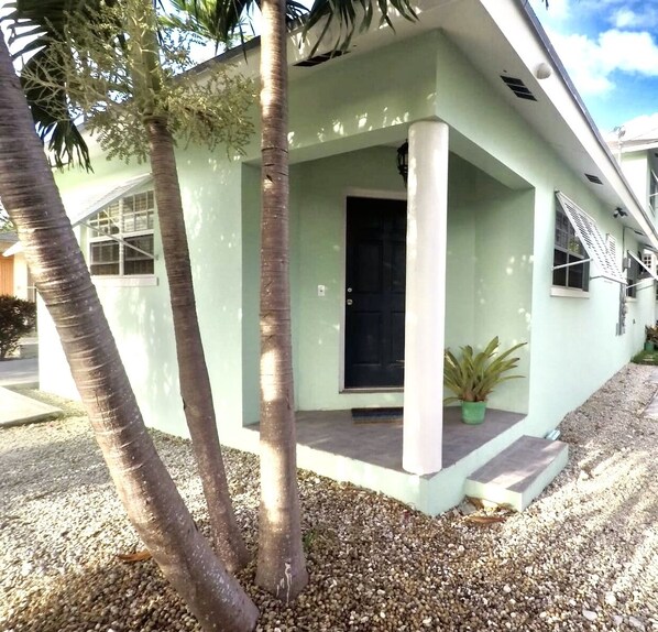 A single-story building with a flat roof, a black front door, and a small porch area with a potted plant.