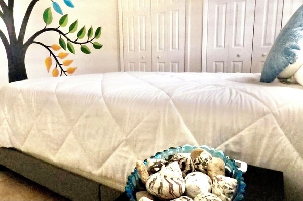 A bedroom with a bed, a wall mural, and a basket of decorative items.