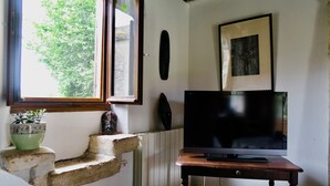 Ett rum med en tv på ett träställ, en krukväxt på en stenframträdande list och ett fönster med utsikt över träd.