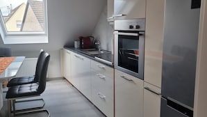 Moderni keittiö, jossa on sisäänrakennettu uuni, ruostumattomasta teräksestä valmistettu jääkaappi ja ikkuna, josta avautuu näkymä asuinalueelle.