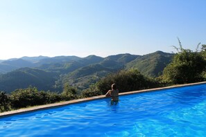 Une personne dans une piscine, avec en arrière-plan une vue sur des collines verdoyantes.