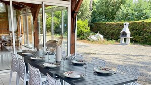 An outdoor dining area with a covered patio, a long table set for six, and a stone oven in the background. - Villa Amandelle - for 6 to 8 persons (Moliets-et-Maa)