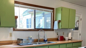 A kitchen with green cabinets, a wooden countertop, a double sink, and a window above the sink. - Quaint Downtown Cottage (Astoria)