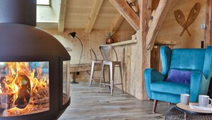 Une pièce chaleureuse avec un poêle à bois, un fauteuil de couleur turquoise et un coin repas comprenant des chaises et une table.
