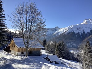 Een houten hut met een stenen fundering, omgeven door met sneeuw bedekte bomen en bergen op de achtergrond.