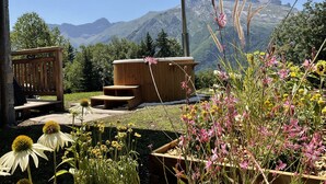 Un espace extérieur aménagé en bois, avec des marches menant à un jacuzzi, entouré de différentes fleurs et offrant une vue sur les montagnes.