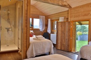 Een slaapkamer in een houten chalet met een douche, twee bedden en uitzicht op de natuur.