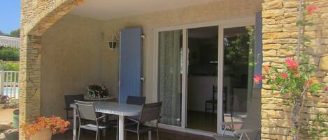 A covered patio with a table and chairs, a potted plant, and a stone wall.
