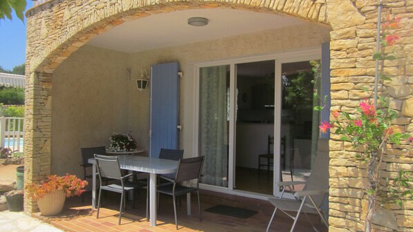 A covered patio with a table and chairs, a potted plant, and a stone wall.