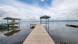 Une jetée en bois mène à un quai sur lequel se trouvent deux structures abritées : l’une contient un bateau, l’autre est vide.