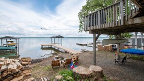 Een terras aan het meer met houten banken en een overdekt gedeelte, liggende boten en een stapel hout.