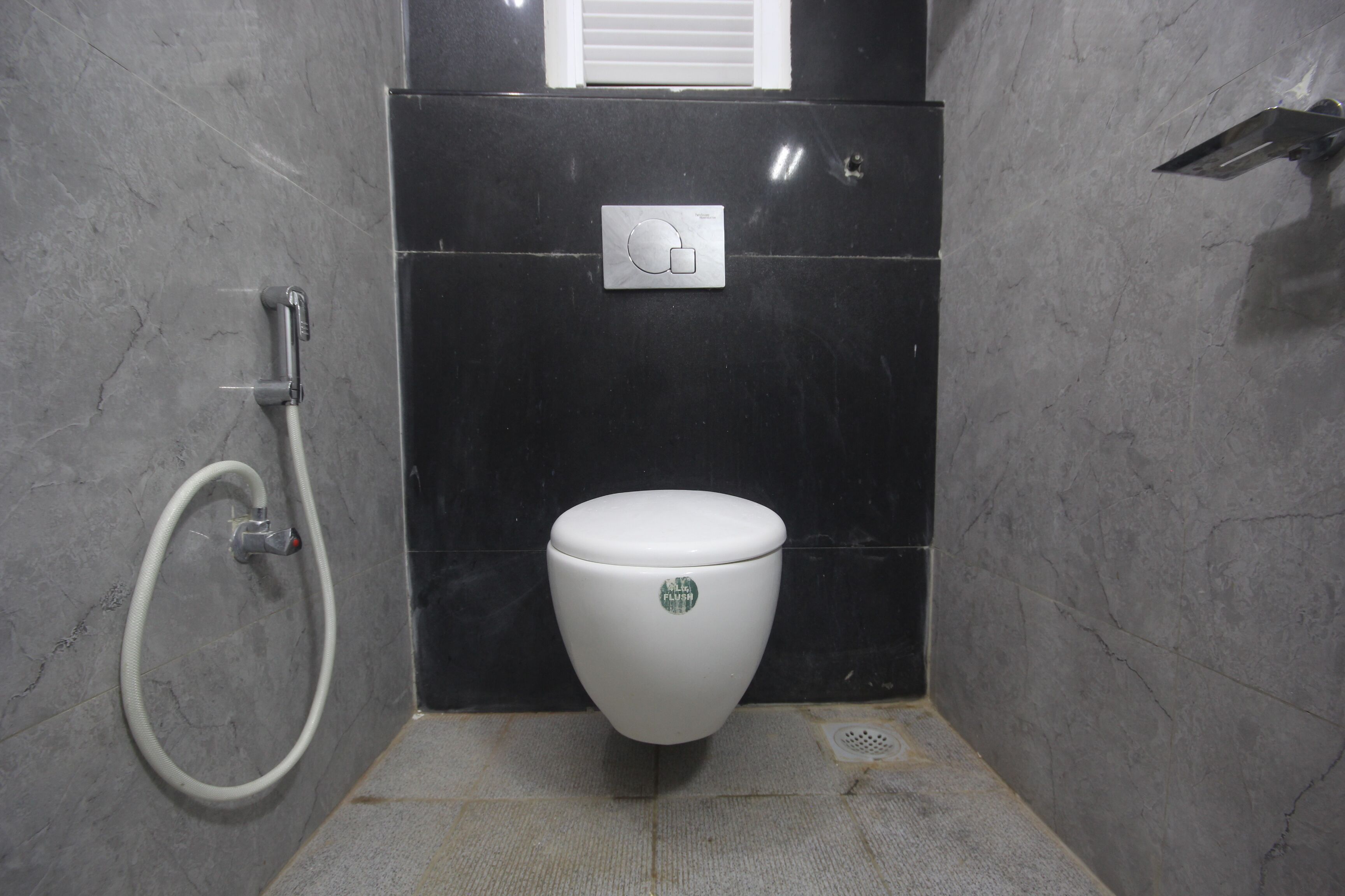 Un baño con inodoro blanco, manguera de ducha y panel de control en la pared.