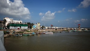 A coastal area with boats docked along the shore, buildings, and a clear sky. - Hotel Prakash (Kilvelur)