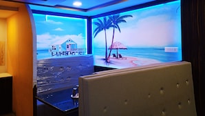 A room with a beach-themed mural, a white cushioned headboard, and a small table with a glass top. - Hotel Prakash (Kilvelur)