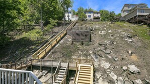 A residential area with wooden staircases leading to houses, surrounded by trees and a rocky terrain.