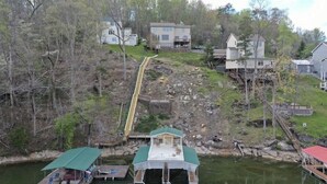 A riverside property with a dock, a small boat, and a wooden bridge connecting to a house.
