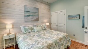 Een slaapkamer met een bed, nachtkastjes, een schilderij van de oceaan en een deur.