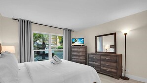 A hotel room with a bed, a dresser, a television, and a large window with curtains. - Renovated Beach Paradise. Ground Floor unit 64 (Longboat Key)