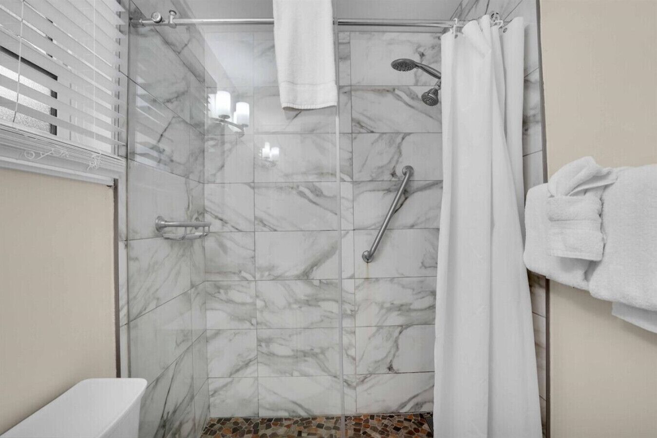 A bathroom with a shower, a handrail, and a towel rack.