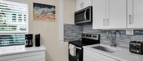 A modern kitchen with white cabinets, a microwave, an oven, a sink, and a toaster.