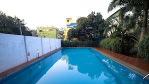Piscina retangular com água azul cristalina, ladeada por um muro branco e uma borda de tijolos vermelhos.
