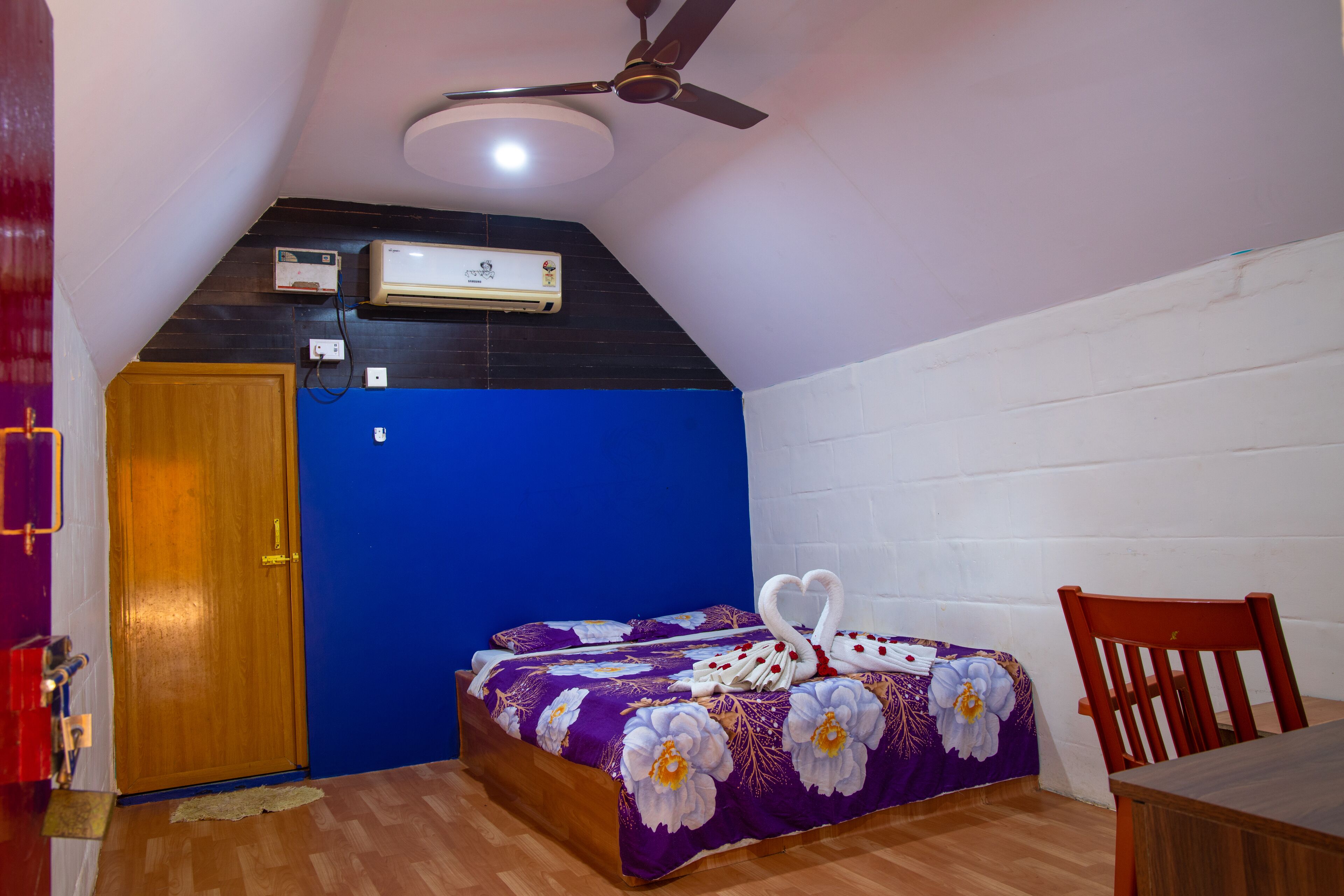 A bedroom with a bed, a ceiling fan, an air conditioning unit, and a wooden door.