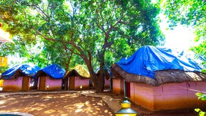 Uma fileira de cabanas com telhado de palha e lonas azuis, um caminho pavimentado e um poste de luz.