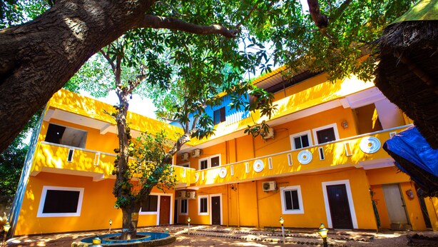 Um edifício amarelo com várias janelas e portas, rodeado por árvores e um pequeno espelho de água circular.