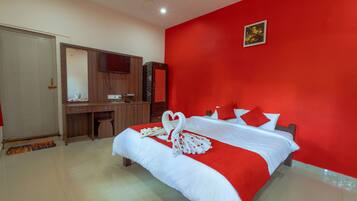 A hotel room with a red accent wall, a bed with white bedding, a wooden desk, and a large mirror.