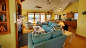 A spacious living room with a large teal sofa, a wooden bookshelf, and a dining area with a view. - Amazing Sound Front, Ocean View Home with Pool, Spa and Dock (Frisco)