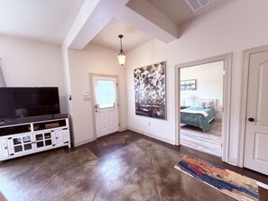 A room with a flat-screen TV, a white entertainment unit, a door leading to a bedroom, and a large abstract painting on the wall. - Chateau 14, spacious townhouse in Tickfaw, LA (Tickfaw)