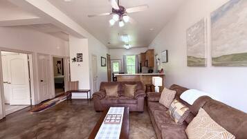 A spacious living room with a brown leather sofa, a coffee table, and a ceiling fan.