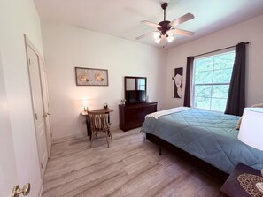 Une chambre à coucher avec un lit, un bureau, une télévision et un ventilateur de plafond.