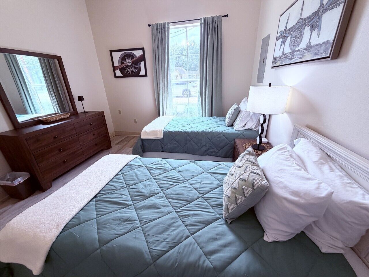 A bedroom with two beds, a dresser, a mirror, and a window with curtains.