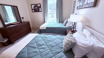 A bedroom with two beds, a dresser, a mirror, and a window with curtains.