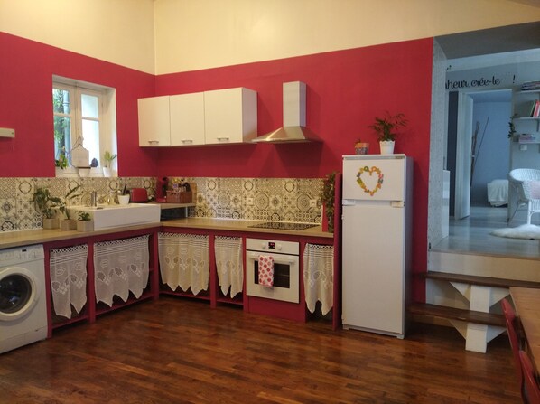 A kitchen with a red wall, white cabinets, a white refrigerator, and a washing machine.