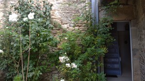 A stone building with a narrow entrance, surrounded by lush greenery and white flowers. - Appartement Nature et Jardin (Eymoutiers)