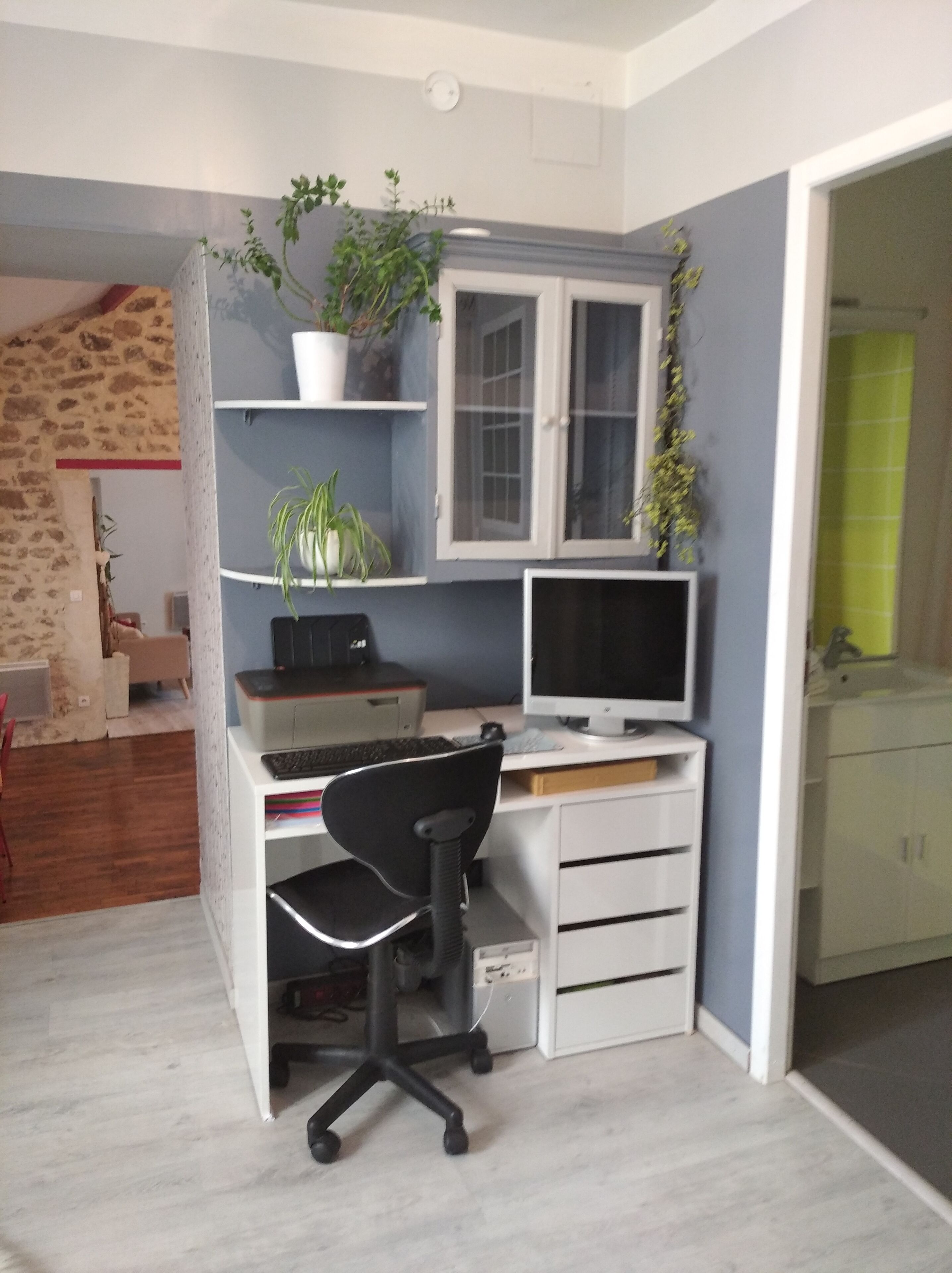 Espacio de oficina compacto con escritorio, silla, computadora, estanterías con plantas y un ventanal pequeño.