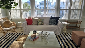 A bright living room with a white sofa, striped rug, and a glass coffee table with books and a vase. - Canal home with access to the Intracoastal Waterway only steps from the beach! (Ocean Isle Beach)