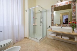 Un baño con ducha envuelta en cristal, un lavamanos blanco y un salpicadero de azulejos.