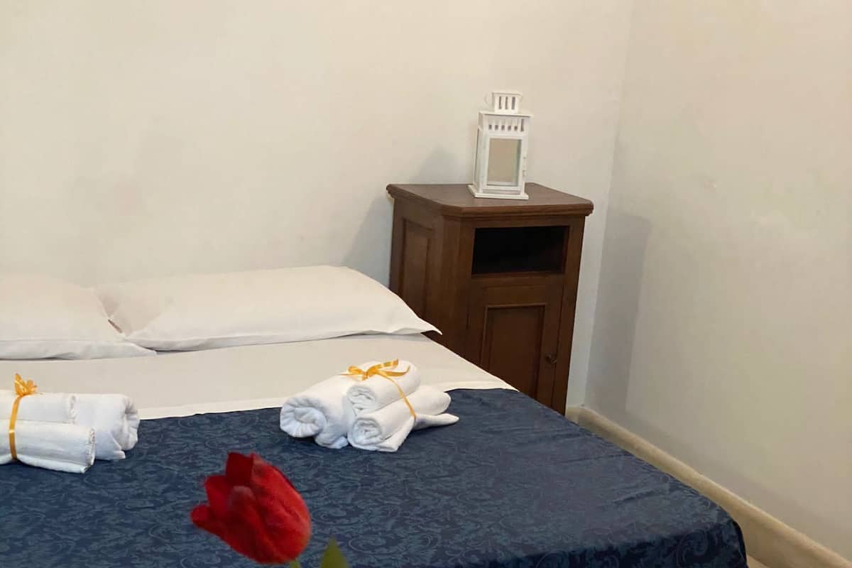 A hotel room with a bed, a nightstand, and a vase with red flowers.